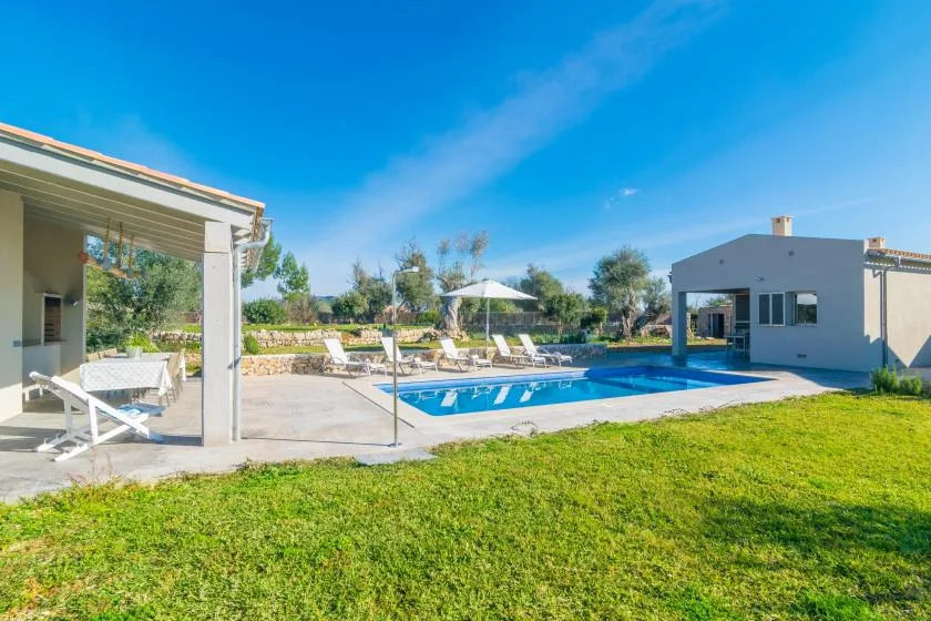 Outdoor swimming pool beside a modern house, with patio seating and a lawn.