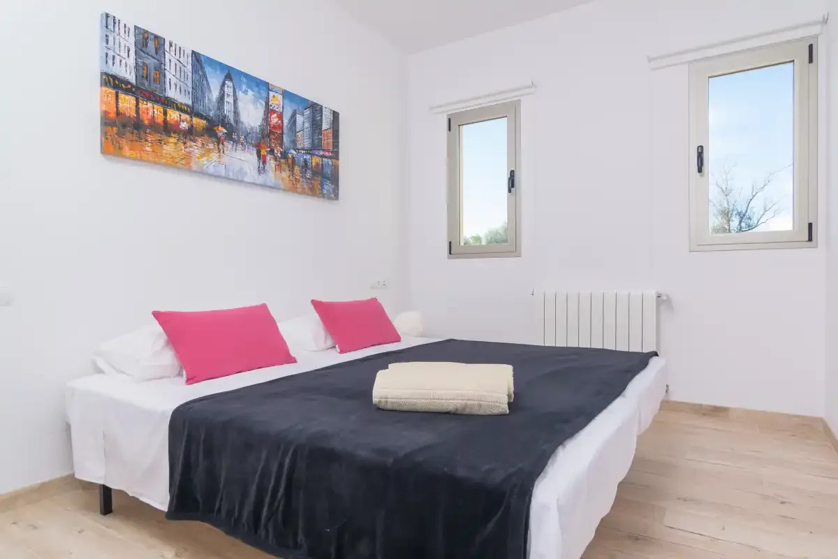 A bedroom with a bed dressed in dark bedding and pink pillows.