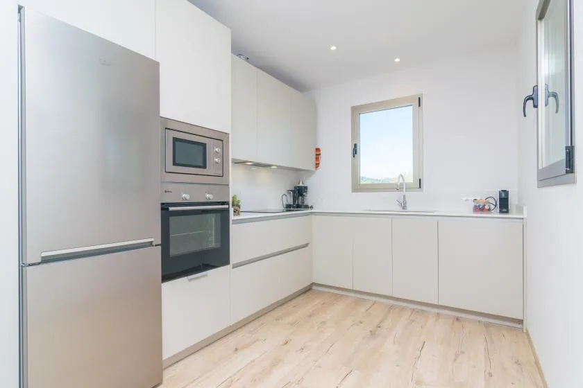 A bright modern kitchen with white cabinets, built-in appliances, and a window above the sink.