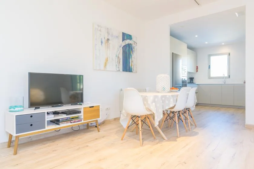A bright dining and living area opens into a kitchen, with a table and television.