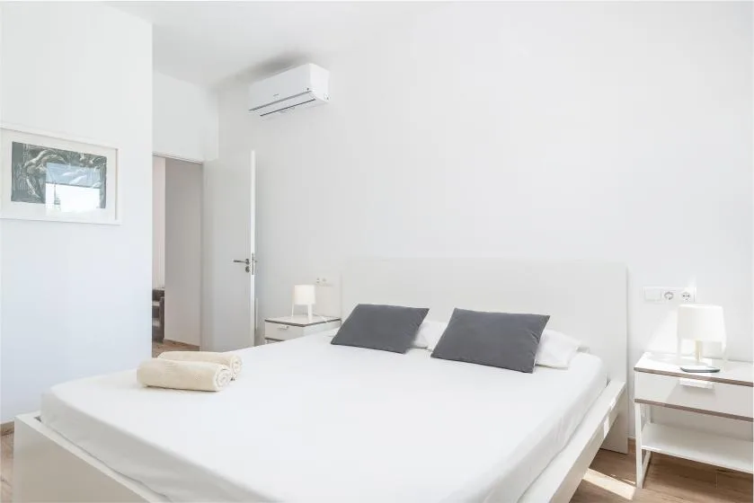 A bright bedroom with a neatly made bed and two dark pillows.