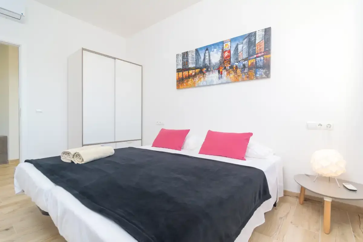 A bright bedroom with a large bed, colorful wall art, and a bedside table.