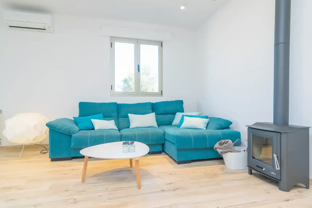 A bright living room has turquoise seating, a round coffee table, and a freestanding stove.