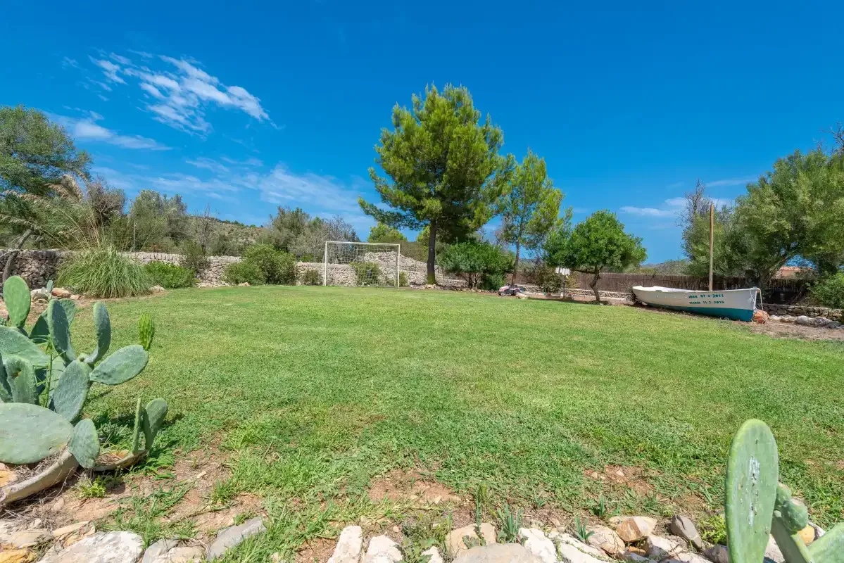 A grassy garden with a soccer goal, trees, and a boat.