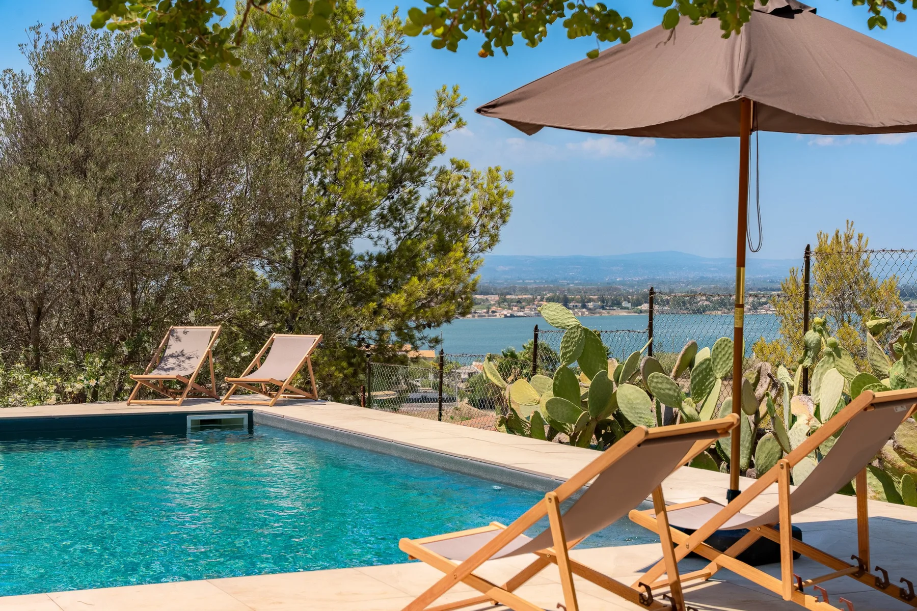Una piscina al aire libre ofrece vistas a un lago, con asientos bajo una sombrilla.