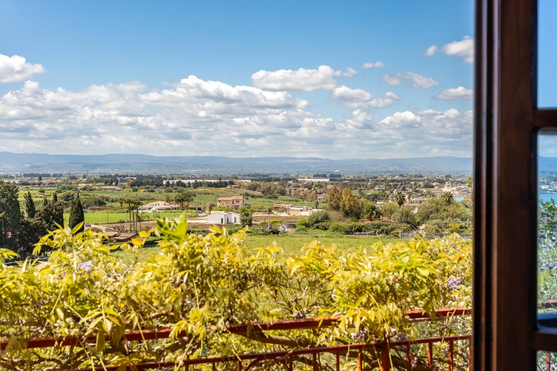 A green valley with scattered buildings stretches beneath a cloudy blue sky.
