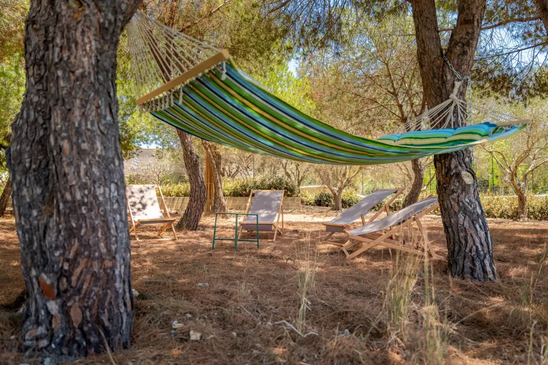 A striped hammock hangs between trees above a shaded outdoor seating area.