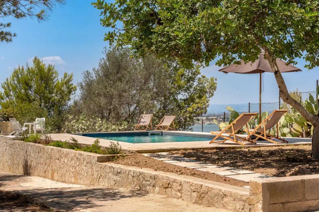 An outdoor swimming pool beside a shaded terrace with lounge seating.