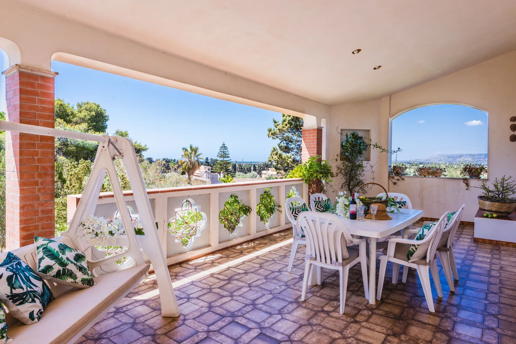 A covered outdoor dining area with a table and chairs overlooking trees and distant buildings.