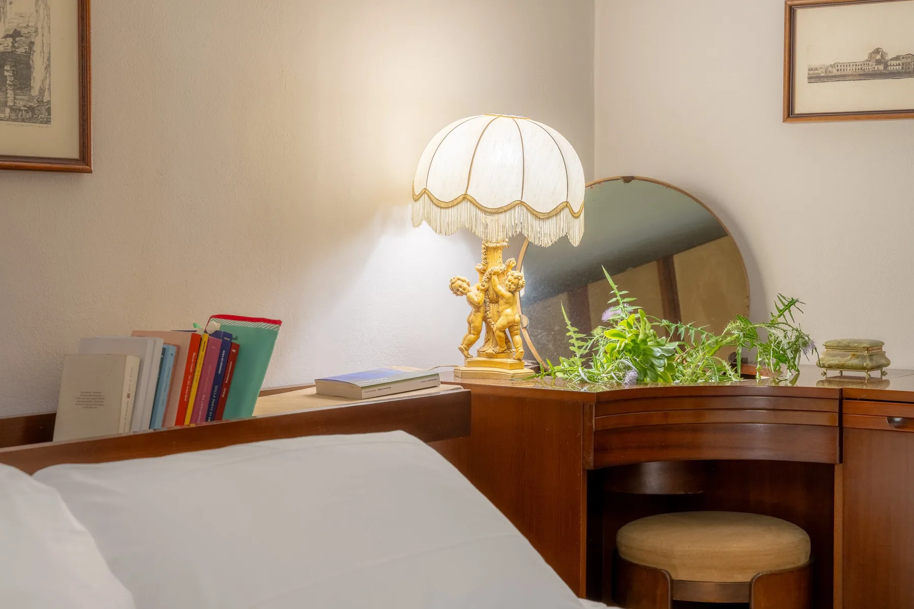 A bedroom with a wooden vanity, a table lamp, and a bed in the foreground.