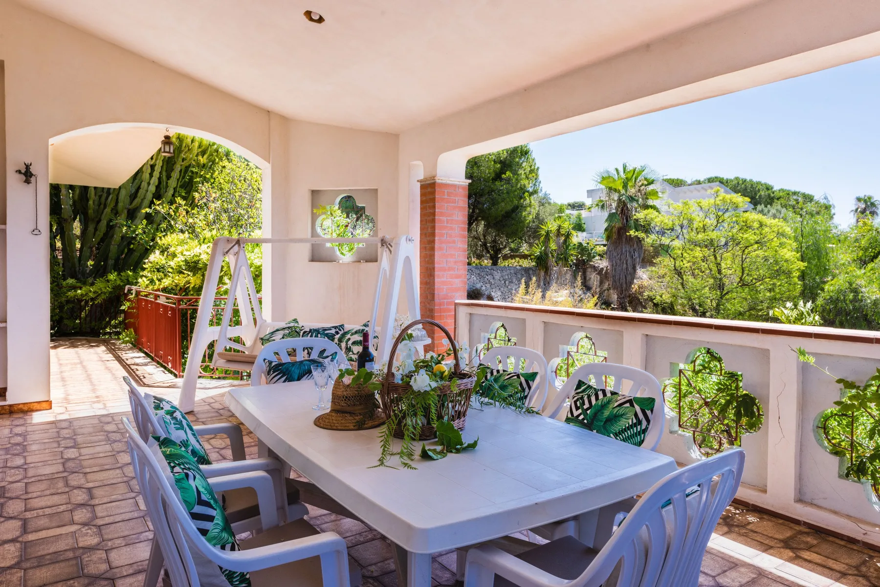 A covered outdoor dining area with a table and chairs overlooks a green garden.