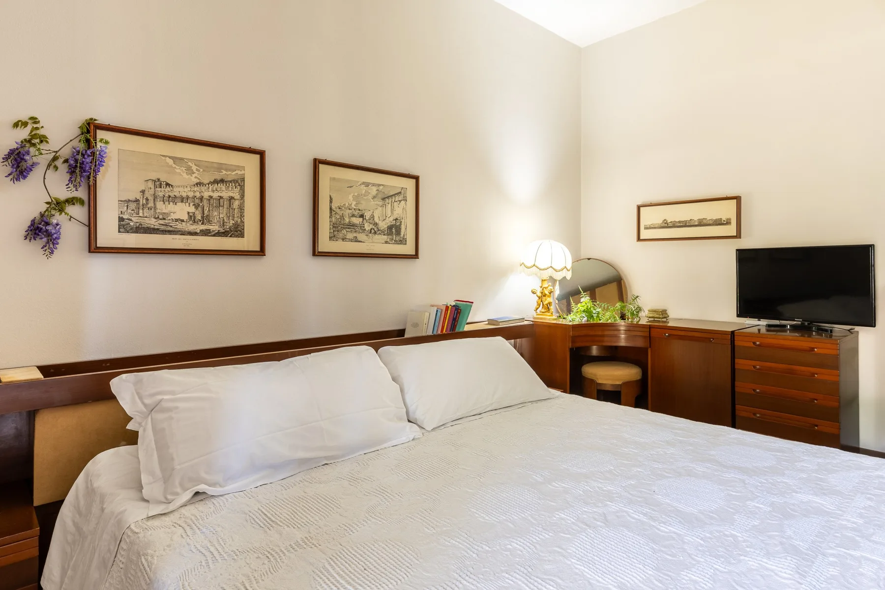 A bedroom with a neatly made bed and a television on a wooden cabinet.