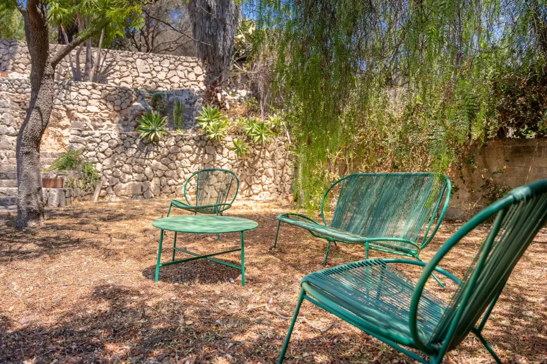 An outdoor seating area with green metal chairs beside a stone wall.