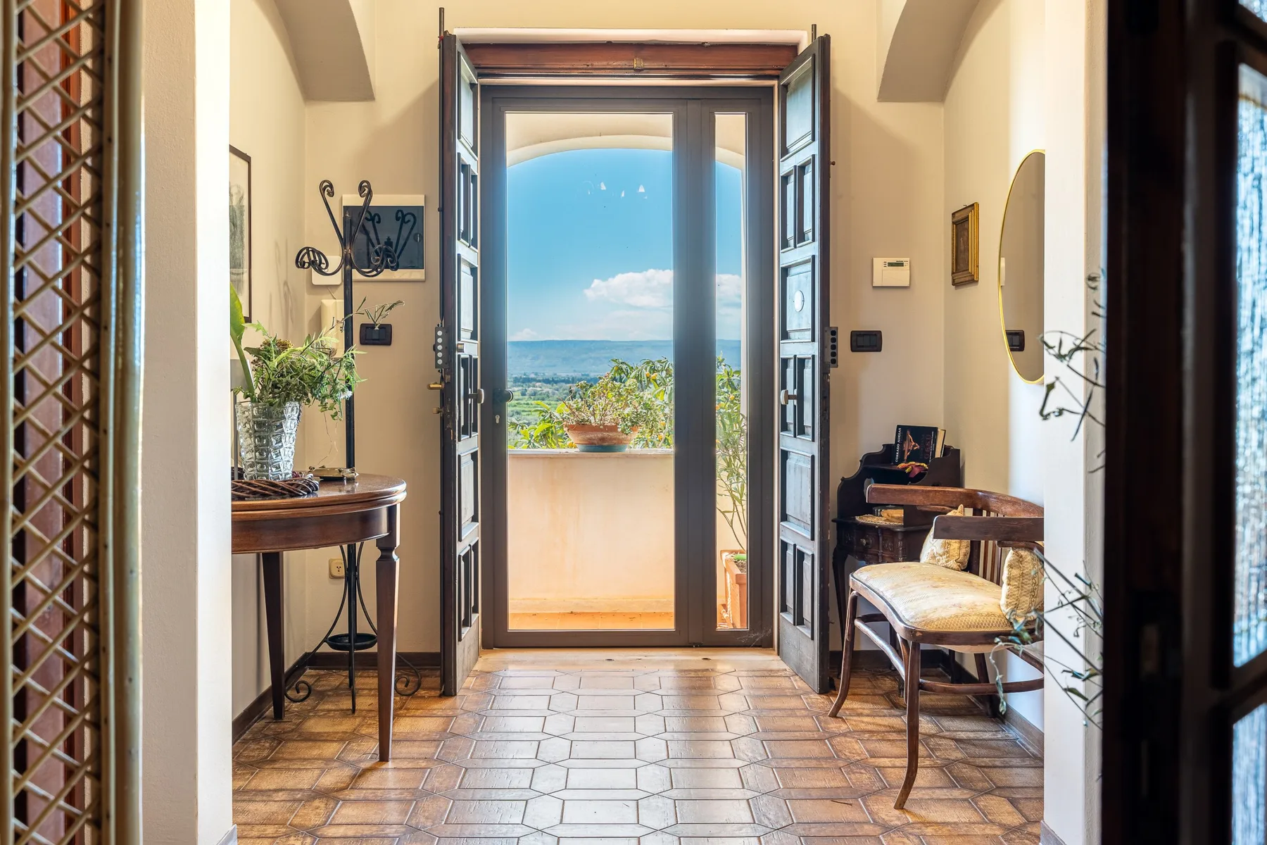 An entry hall opens through a doorway to a terrace with a distant landscape.