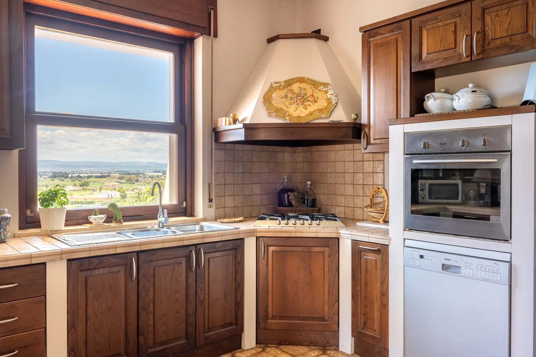 A kitchen with wooden cabinets, a cooktop, and a window overlooking the landscape.
