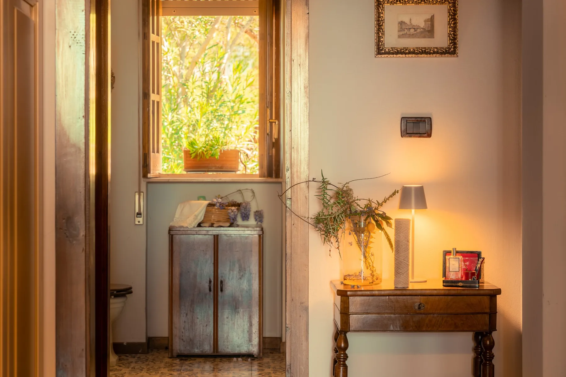 A warmly lit interior hallway with a small cabinet beneath an open window.
