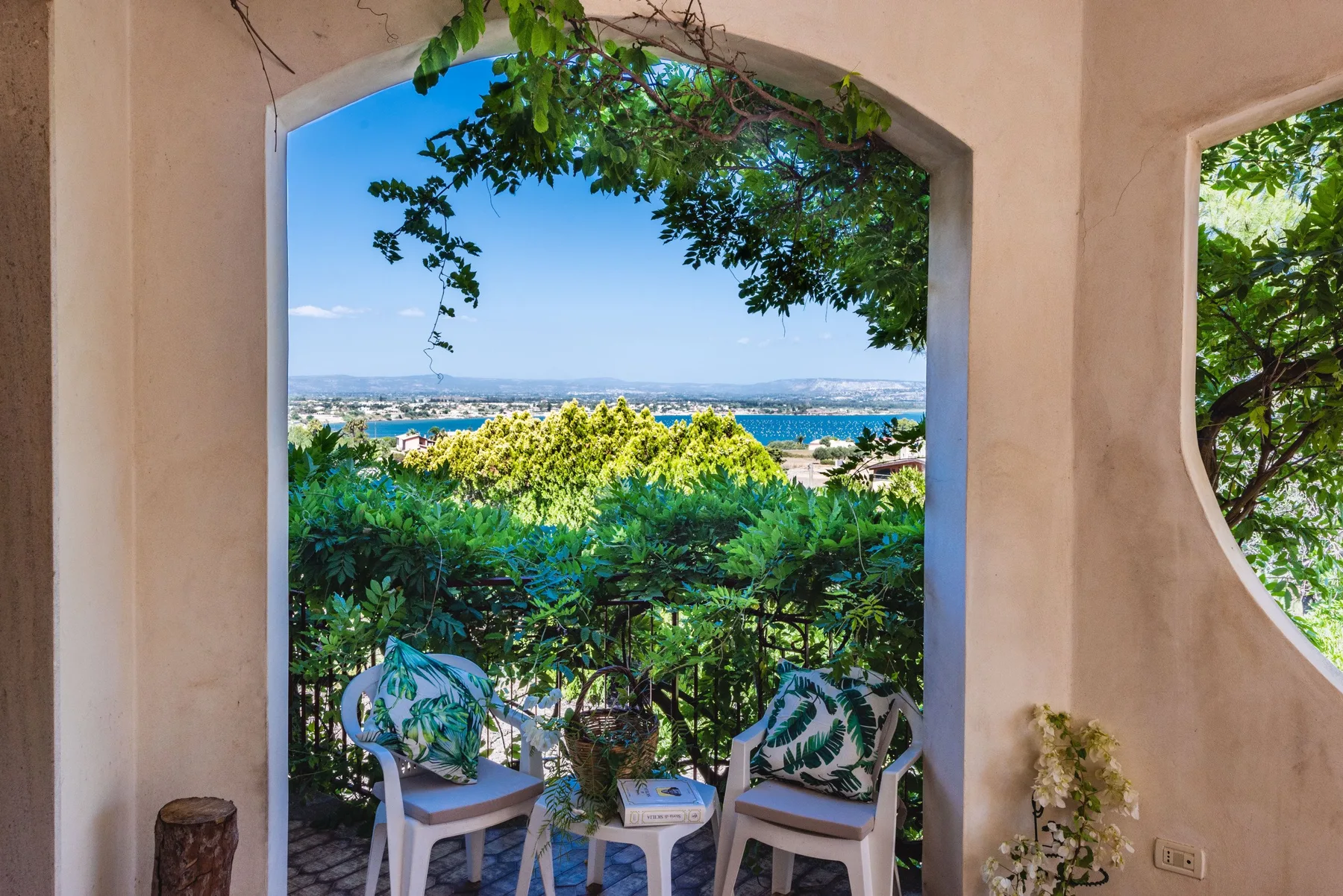 A shaded outdoor seating area overlooks greenery and a distant body of water.