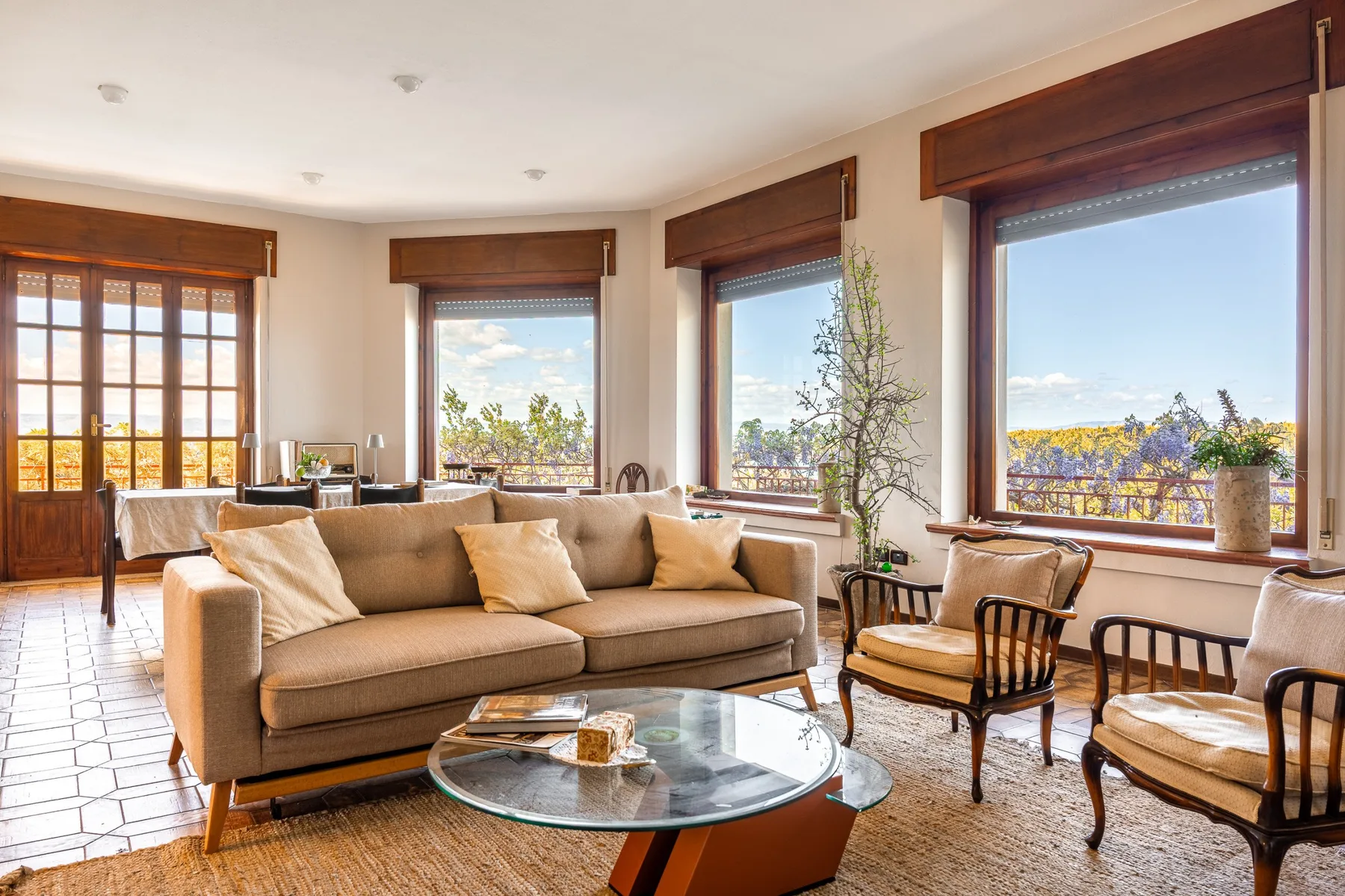 A bright living room with seating arranged around a glass coffee table and large windows.