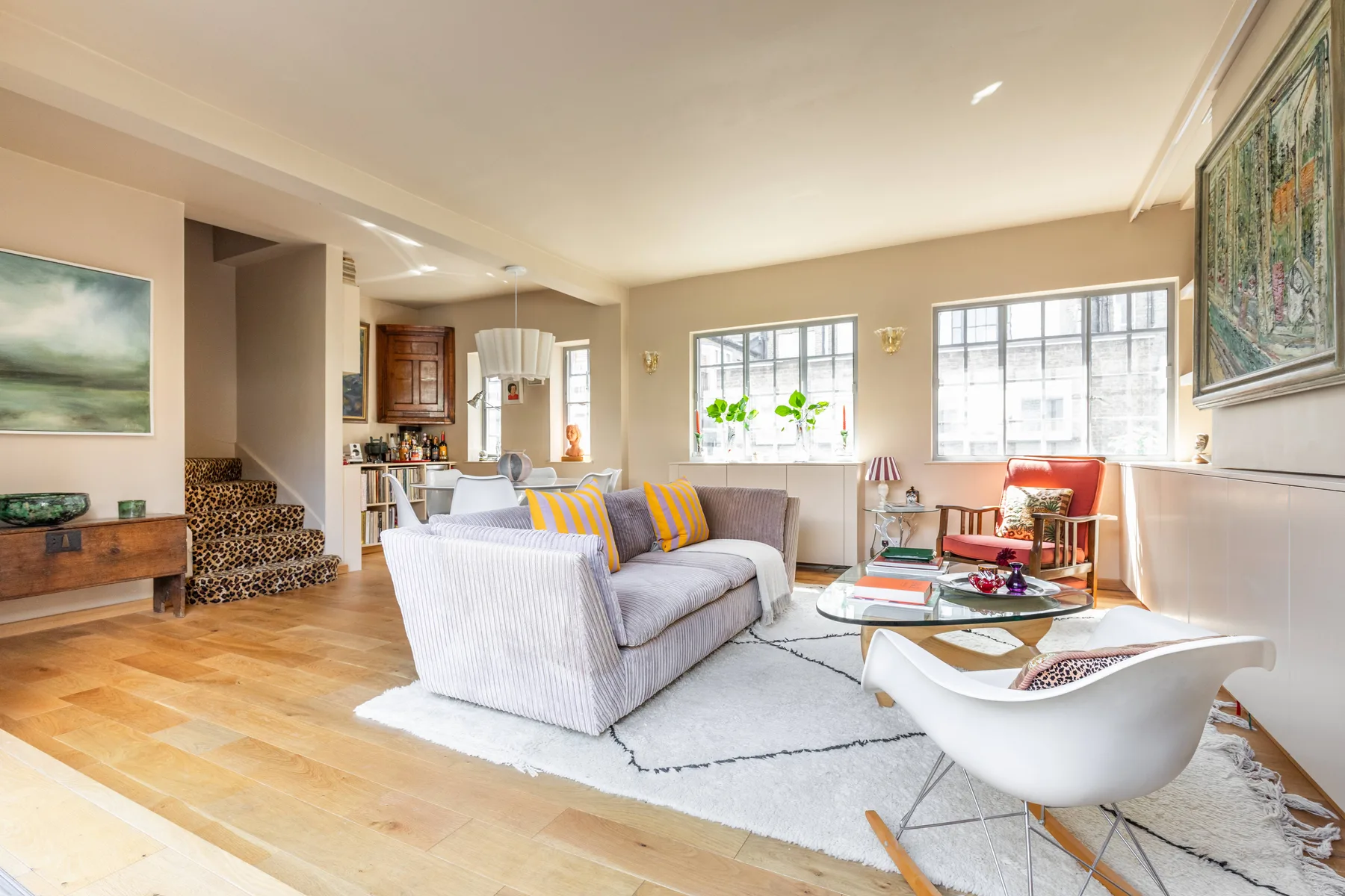 A bright living room with seating, large windows, and a pale area rug.