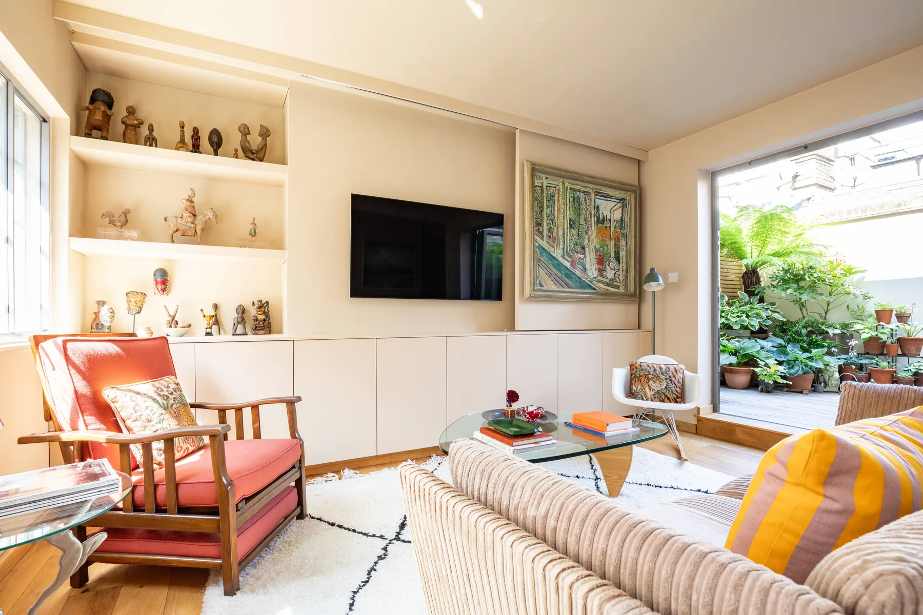 A bright living room with a television, seating, and an open view to a leafy patio.