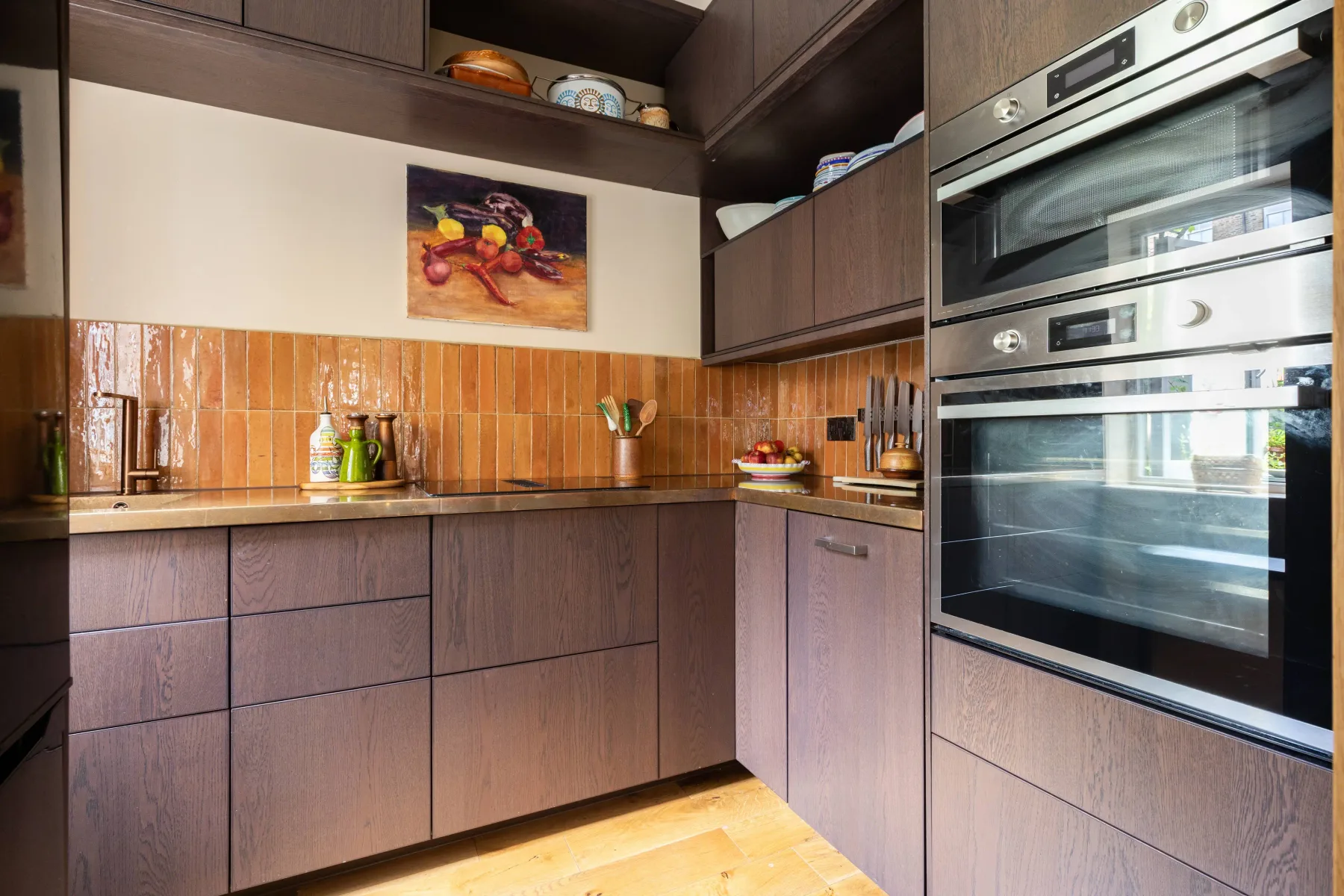 A modern kitchen with dark cabinets, tiled backsplash, and built-in ovens.