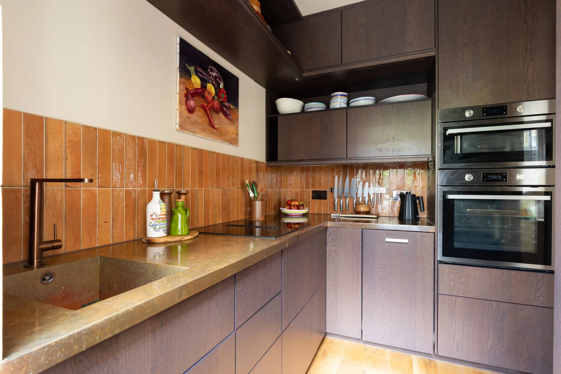 A modern kitchen with dark cabinetry, a countertop sink, and built-in ovens.