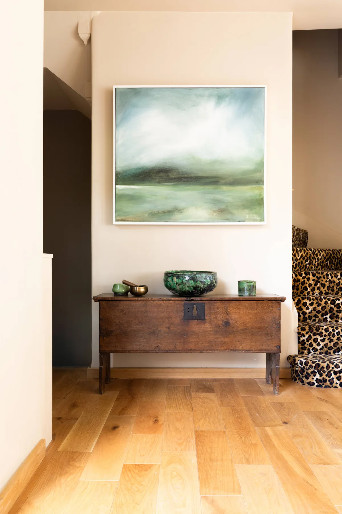 A wooden console table and framed landscape painting decorate a warm-toned interior.