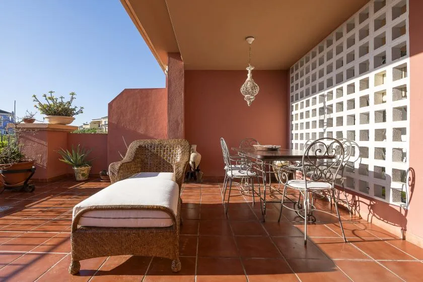 A covered terrace with outdoor seating, a table, and potted plants.