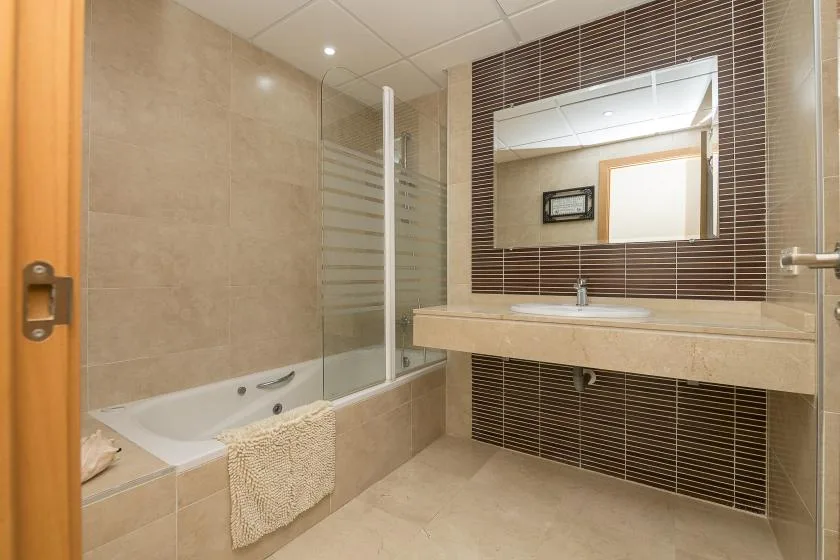 A tiled bathroom with a bathtub, glass shower screen, and broad vanity.