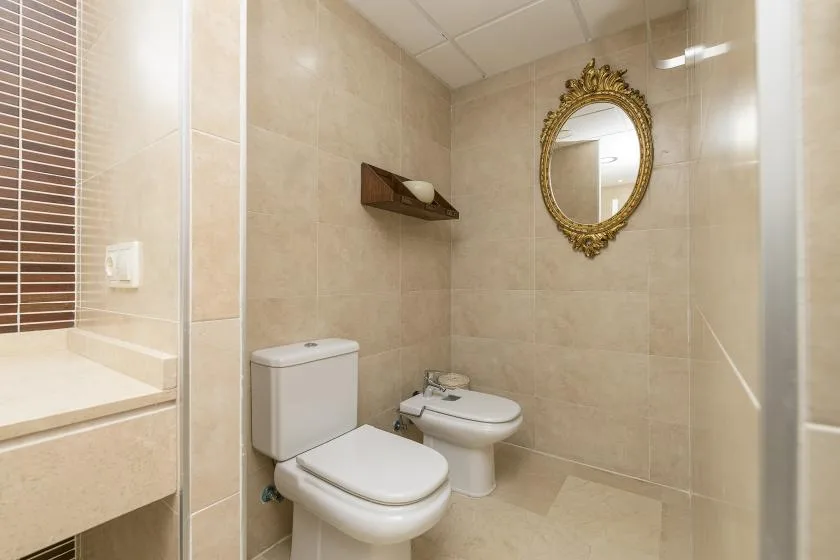 A tiled bathroom with a toilet, sink, and decorative wall mirror.