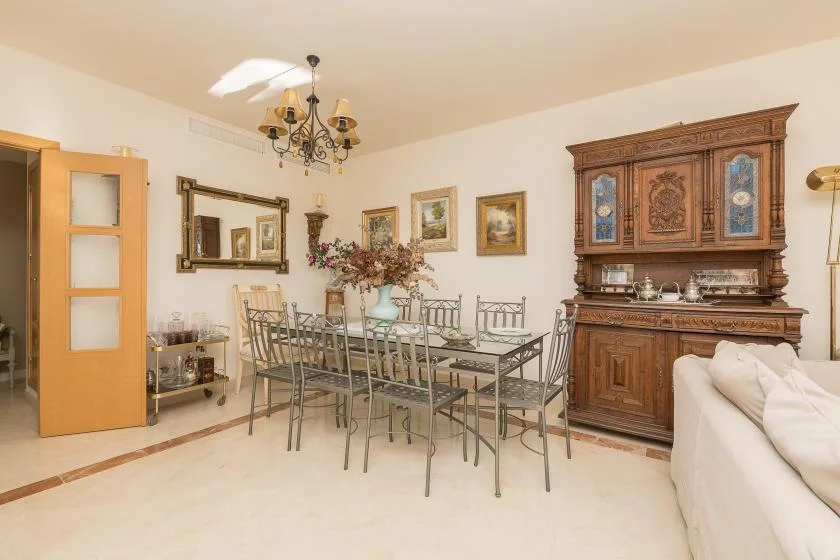A dining room with a glass-topped table, metal seating, and a large wooden cabinet.