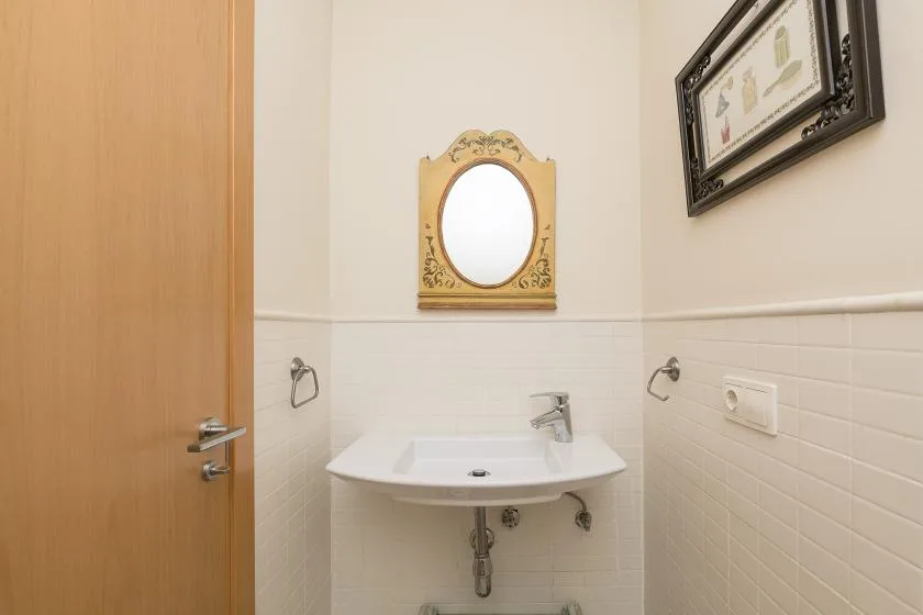 A small bathroom with a wall-mounted sink and oval mirror.