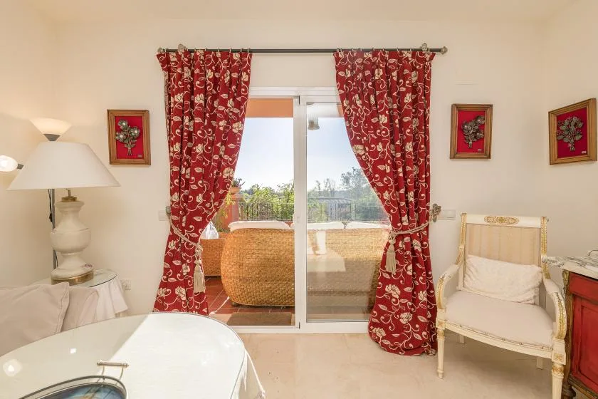 A bright sitting room with red patterned curtains framing a glass door.