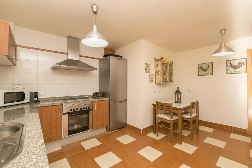 A kitchen and dining area with wooden cabinetry, a table, and tiled flooring.