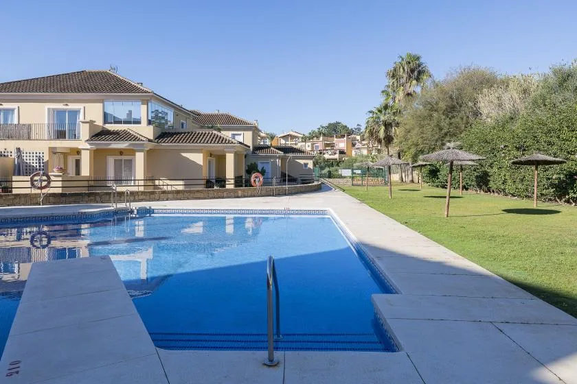 An outdoor swimming pool beside a grassy lawn and nearby residential buildings.