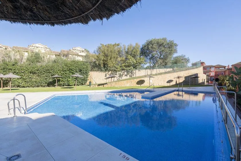 An outdoor swimming pool sits beside a paved deck and landscaped grounds.