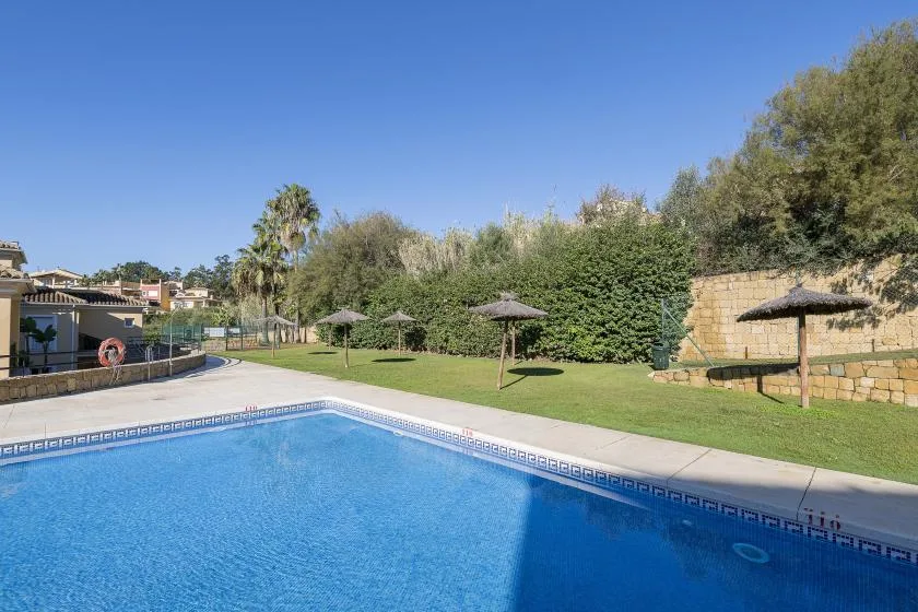 An outdoor swimming pool borders a grassy area with several shaded seating spots.