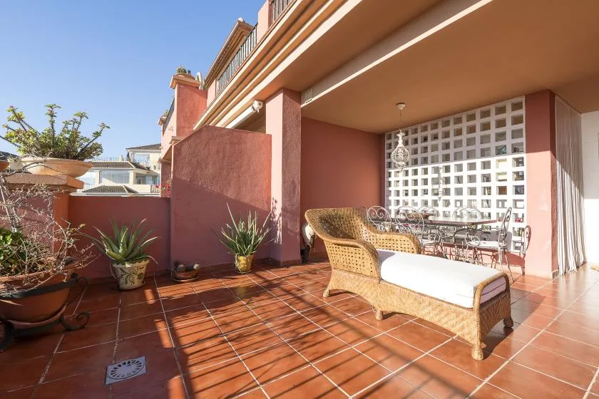 A sunny tiled terrace with wicker seating and potted plants.