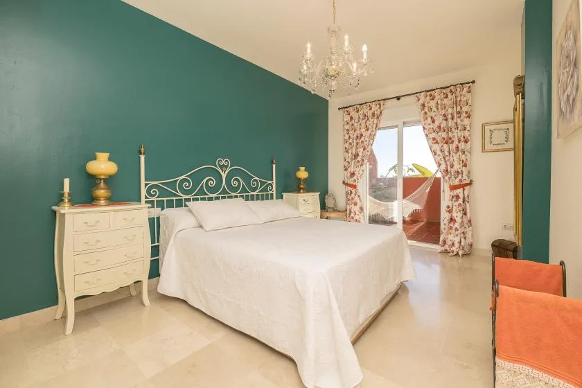 A bright bedroom with a white bed, teal wall, and curtained balcony doors.