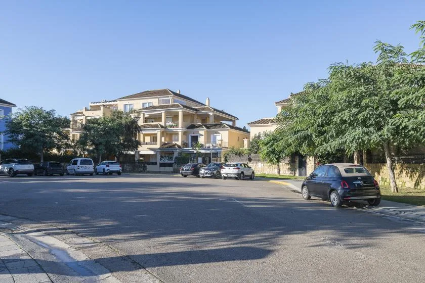 A paved parking area in front of a multi-story building, with several parked cars.