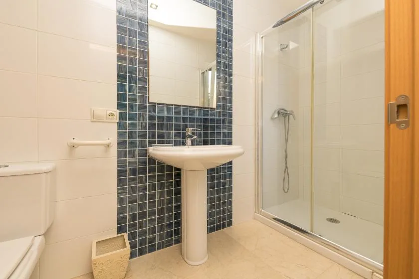 A tiled bathroom with a pedestal sink and glass shower.