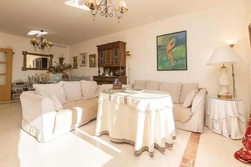A bright living room with pale seating arranged around a covered coffee table.
