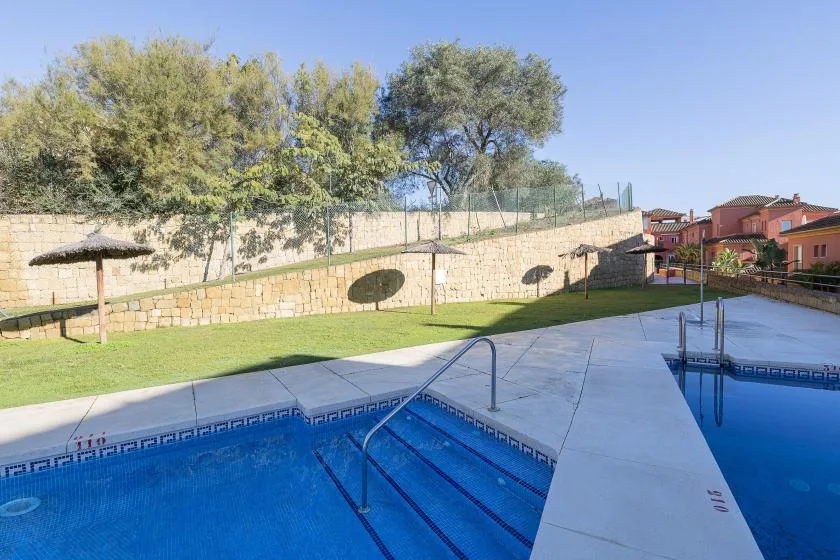 An outdoor swimming pool sits beside a paved deck and grassy lawn.