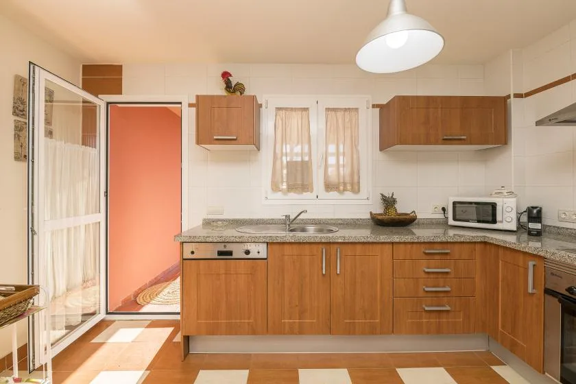 A kitchen with wooden cabinets, a countertop, and a small curtained window.