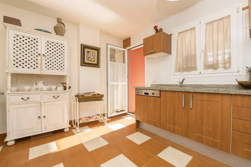 A bright kitchen with wooden cabinets, a sink, and patterned floor tiles.