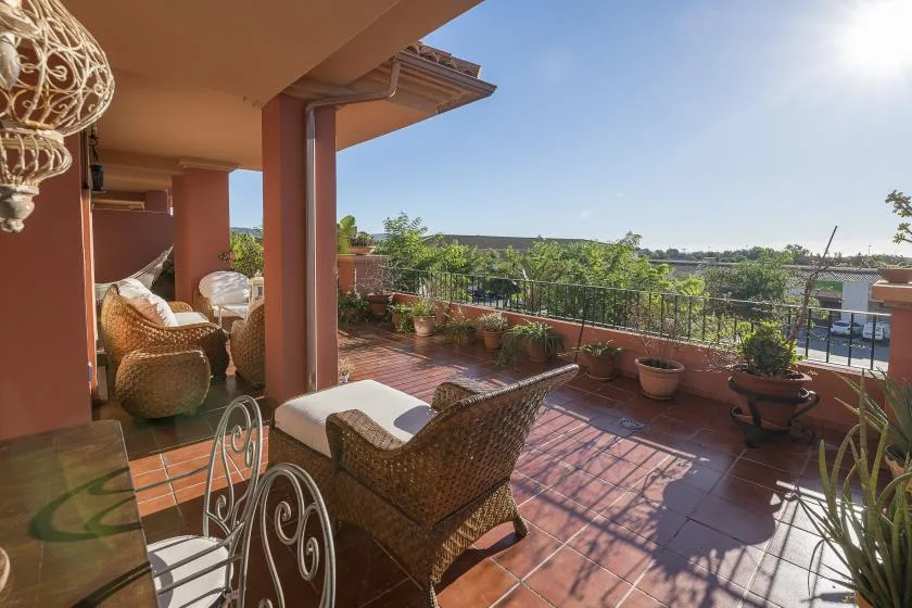 A sunny terrace with wicker seating, potted plants, and views over nearby rooftops.