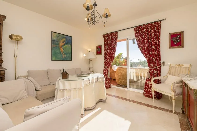 A bright living room with seating around a table beside a glass door and patterned curtains.
