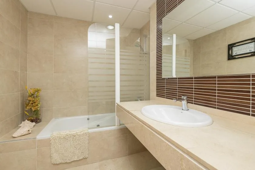 A tiled bathroom with a bathtub, shower, and sink beneath a large mirror.
