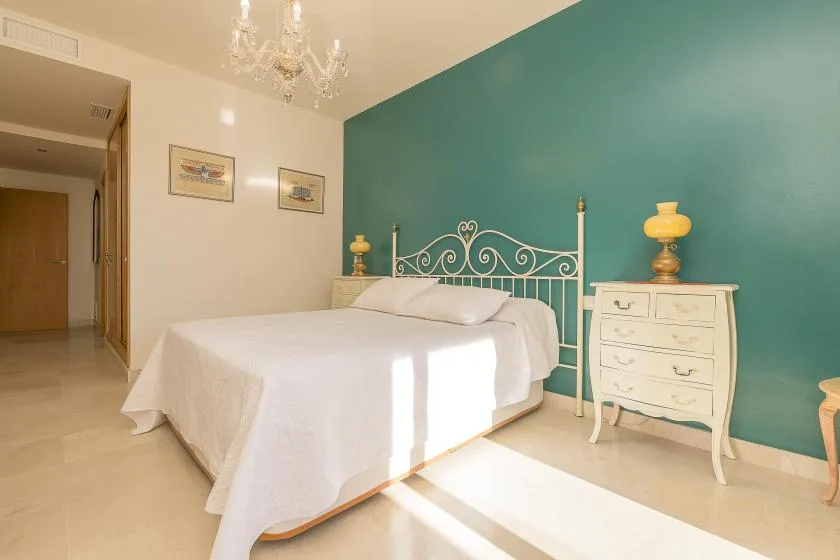 A bright bedroom with a white bed against a teal wall.