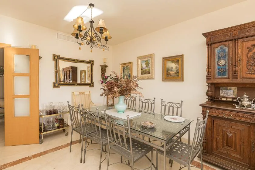 A dining room with a glass-top table, metal seating, and a wooden cabinet.